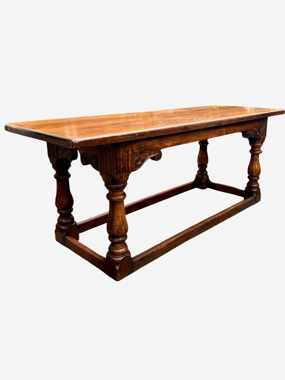 A mid-Victorian solid oak refectory table featuring turned baluster legs, a carved frieze, and a low perimeter stretcher.
