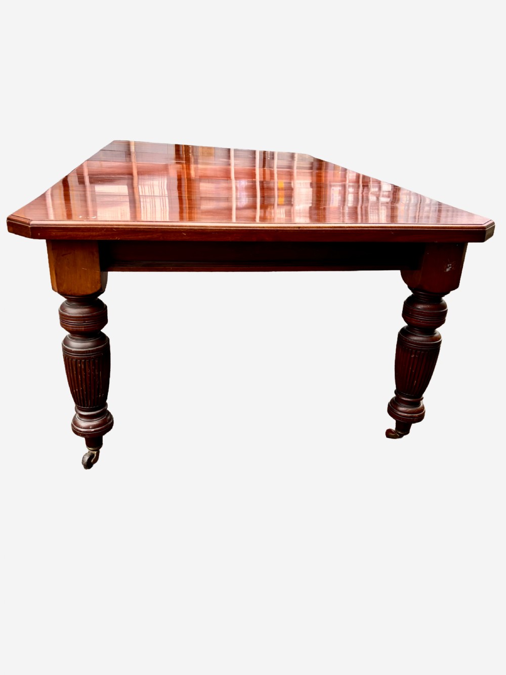 An Edwardian mahogany extending dining table featuring a polished rectangular surface, substantial turned reeded legs, and brass castors.