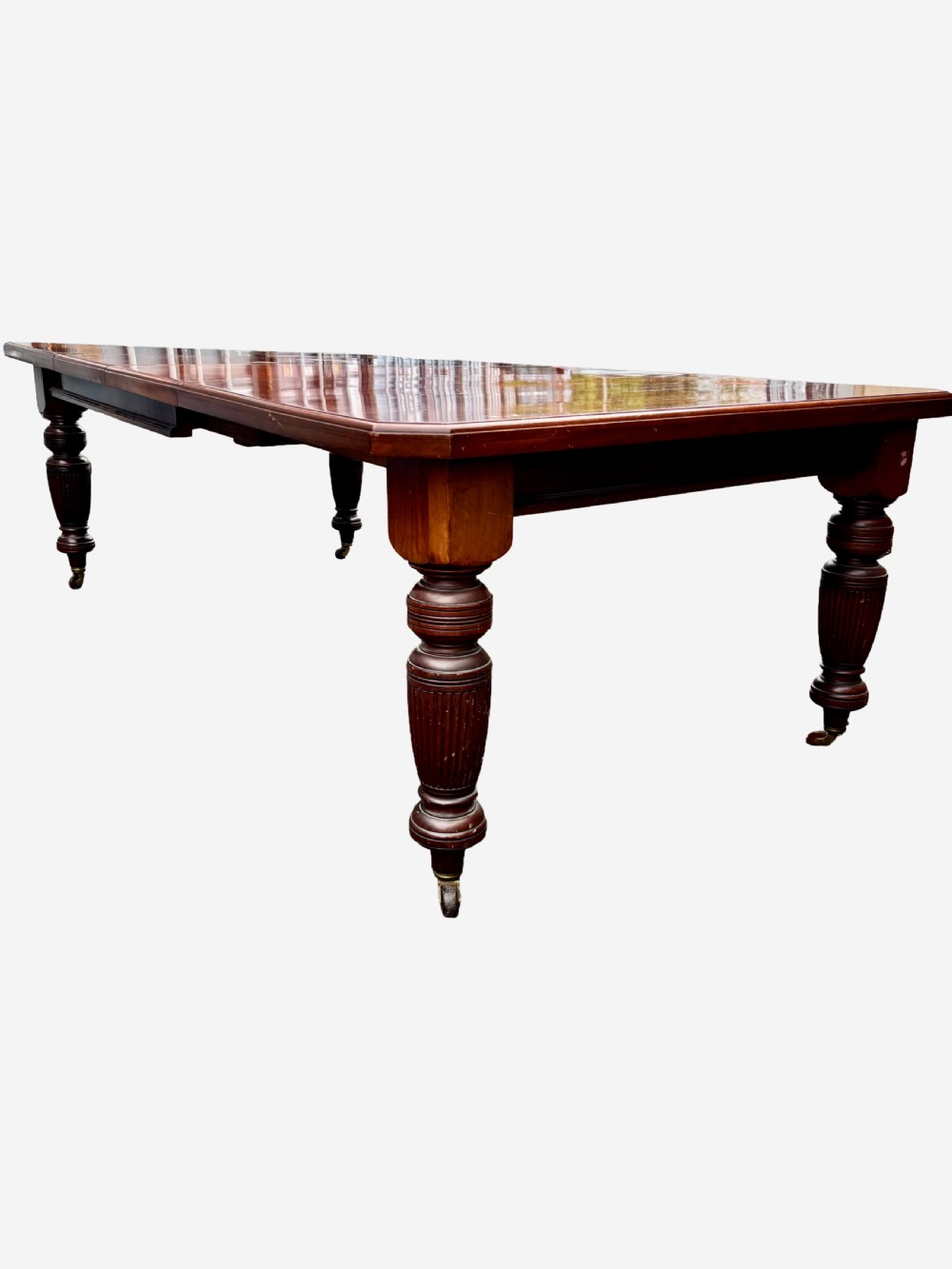 An Edwardian mahogany extending dining table featuring a polished rectangular surface, substantial turned reeded legs, and brass castors. View II