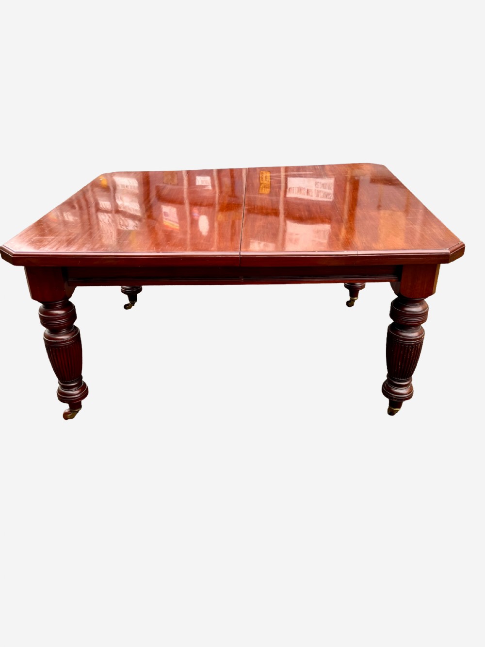 An Edwardian mahogany extending dining table featuring a polished rectangular surface, substantial turned reeded legs, and brass castors. View III