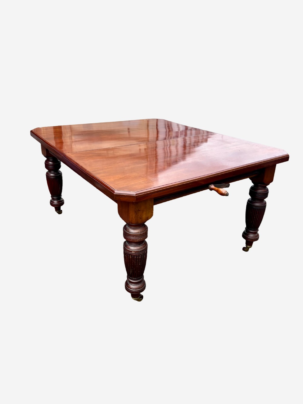 An Edwardian mahogany extending dining table featuring a polished rectangular surface, substantial turned reeded legs, and brass castors. View IV