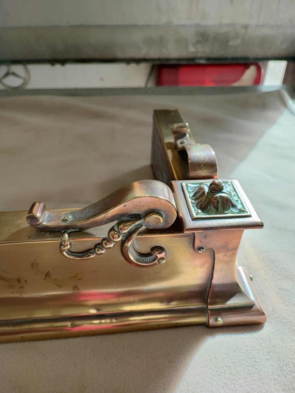 An elongated Victorian brass and copper fireplace fender featuring raised scrollwork mounts and decorative corner detailing. View III