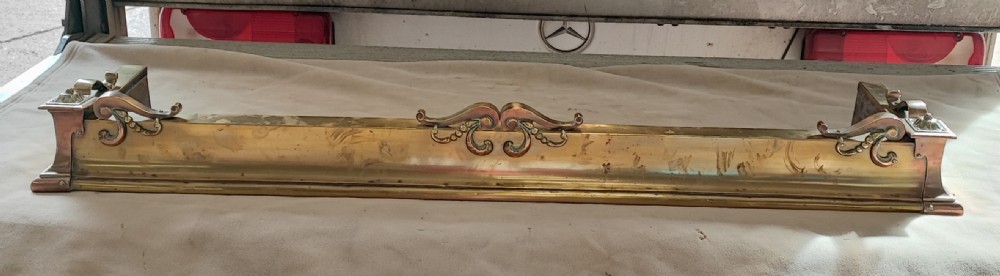 An elongated Victorian brass and copper fireplace fender featuring raised scrollwork mounts and decorative corner detailing. View VI