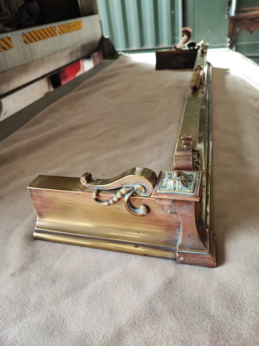 An elongated Victorian brass and copper fireplace fender featuring raised scrollwork mounts and decorative corner detailing. View VII