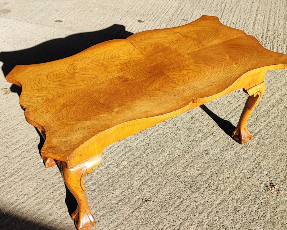 An antique walnut coffee table featuring a serpentine-shaped top with figured grain, supported by four cabriole legs ending in carved ball and claw feet.