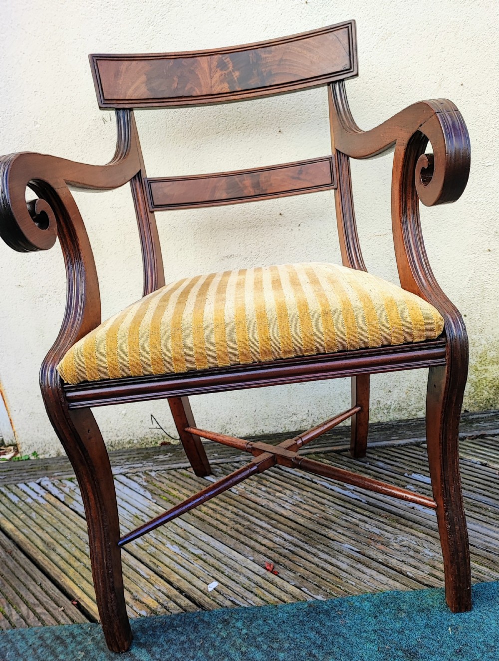 A Regency mahogany armchair featuring curved scroll arms, sabre legs, cross stretchers, and a yellow striped fabric seat.