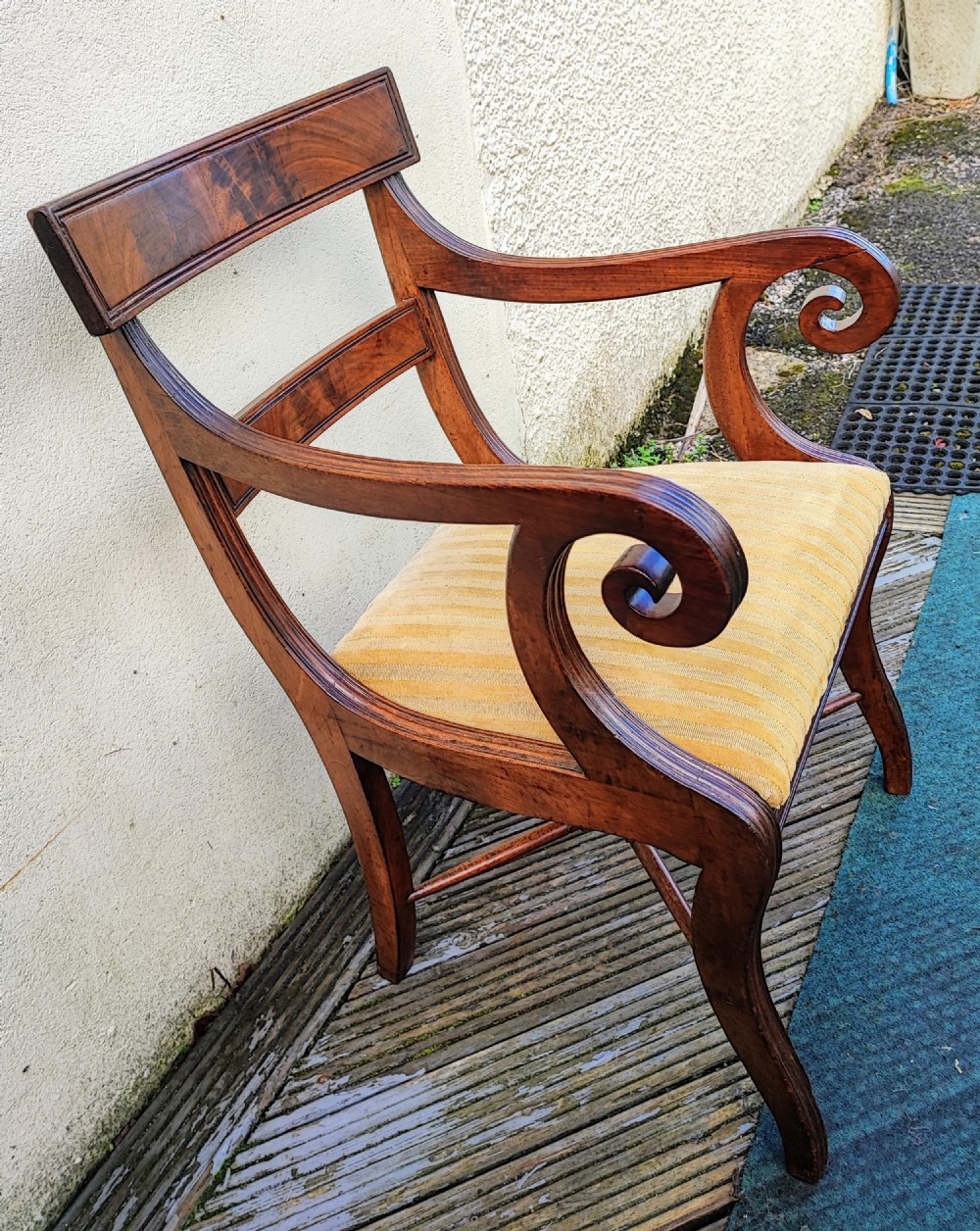 A Regency mahogany armchair featuring curved scroll arms, sabre legs, cross stretchers, and a yellow striped fabric seat. View III