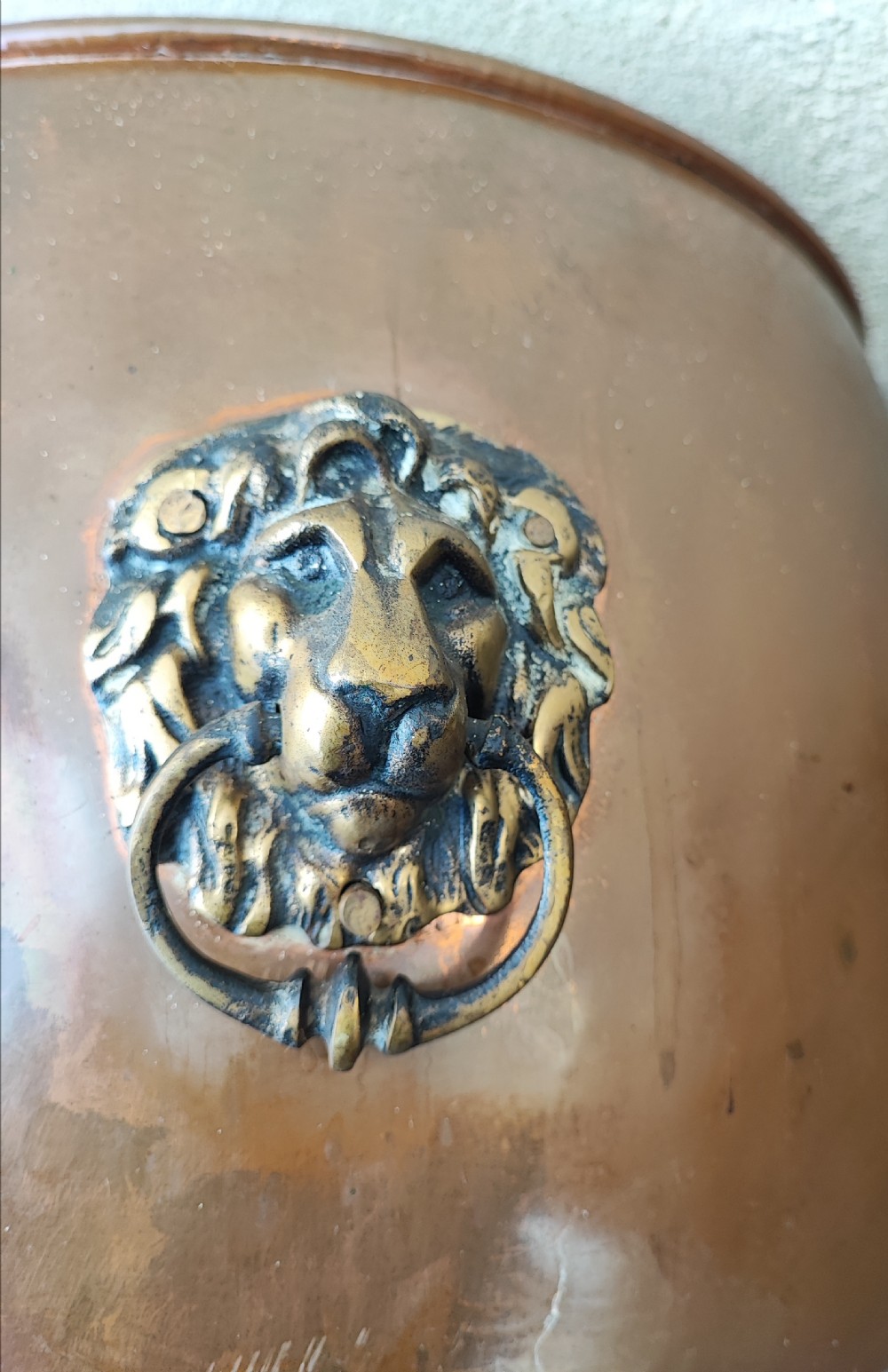 A deep cylindrical copper log bin featuring riveted side seams, brass lion-mask drop-ring handles, and raised paw feet. View V