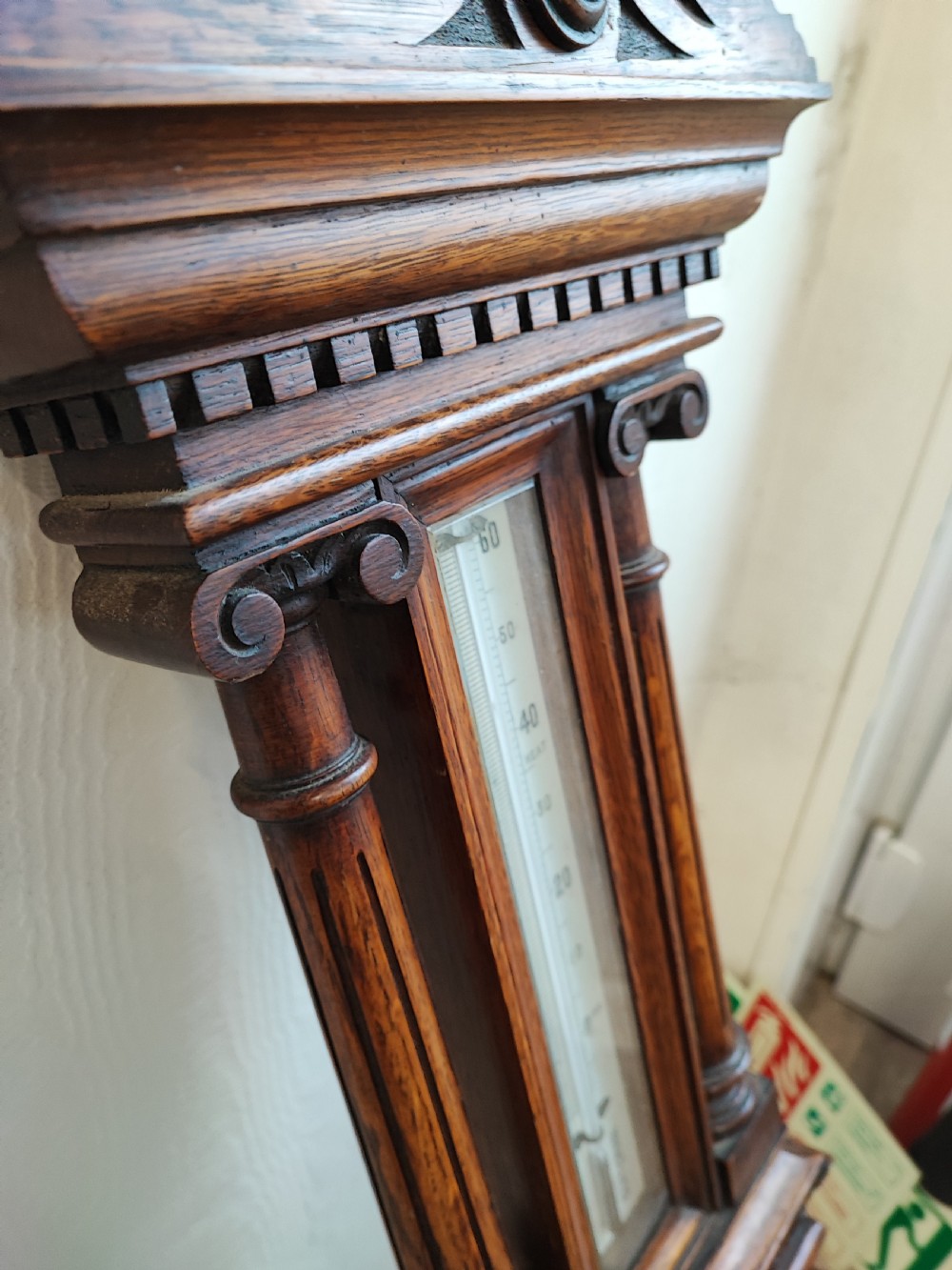 A carved oak wall barometer featuring an upper thermometer flanked by turned columns above a circular aneroid dial. View II