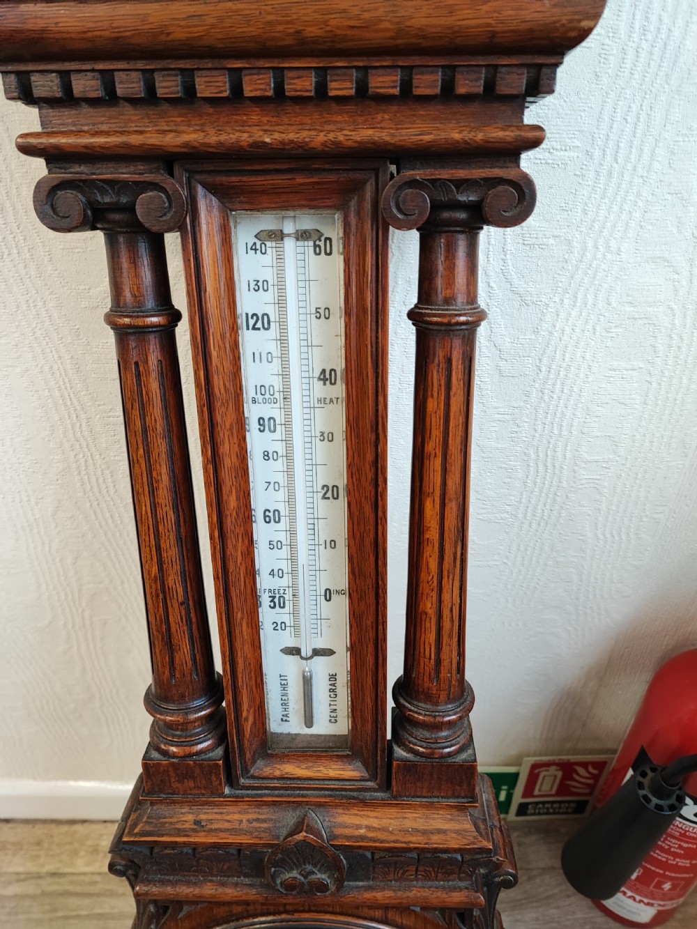 A carved oak wall barometer featuring an upper thermometer flanked by turned columns above a circular aneroid dial. View III