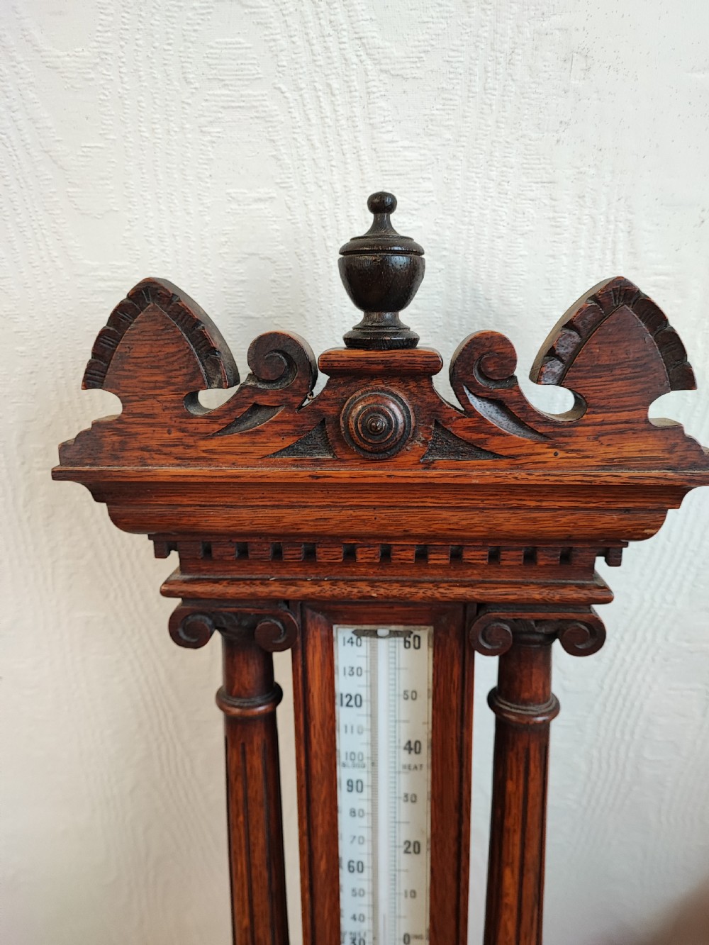 A carved oak wall barometer featuring an upper thermometer flanked by turned columns above a circular aneroid dial. View IV