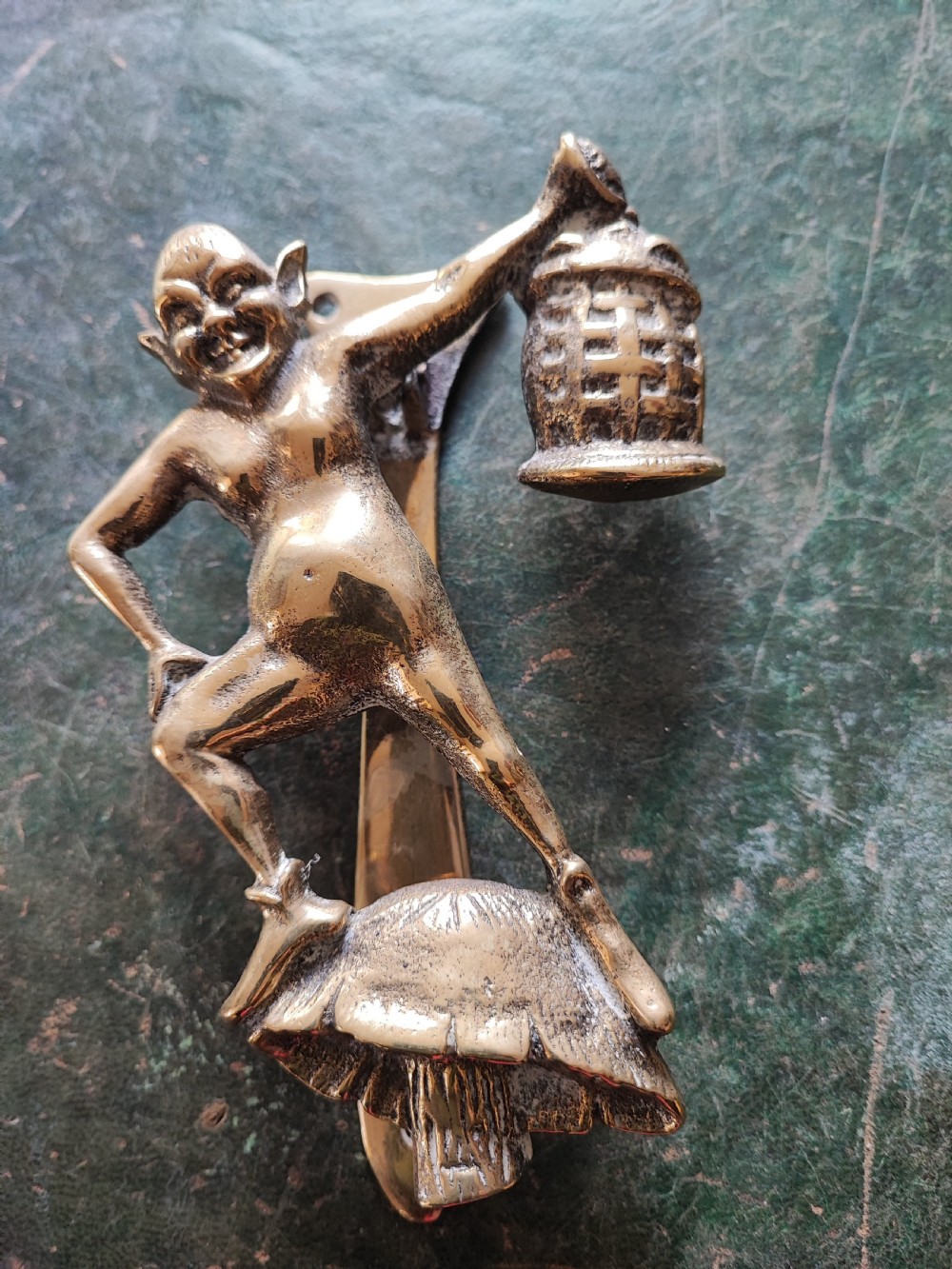 An antique solid brass door knocker sculpted in the shape of a whimsical imp holding a lantern while standing atop a mushroom base. View VIII