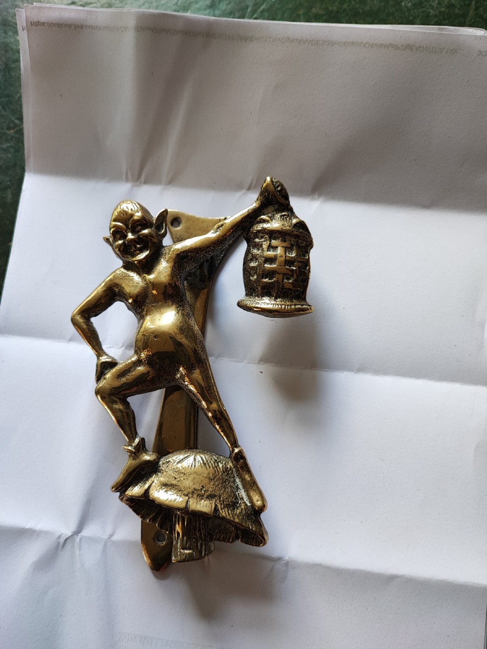 An antique solid brass door knocker sculpted in the shape of a whimsical imp holding a lantern while standing atop a mushroom base. View XV