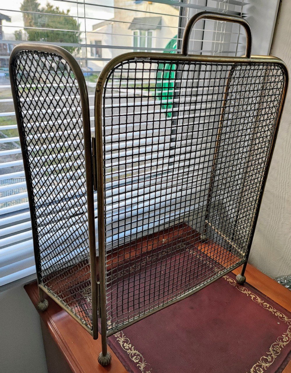 A Victorian brass spark guard featuring a central woven mesh panel with an arched handle, flanked by two hinged side wings on ball feet.