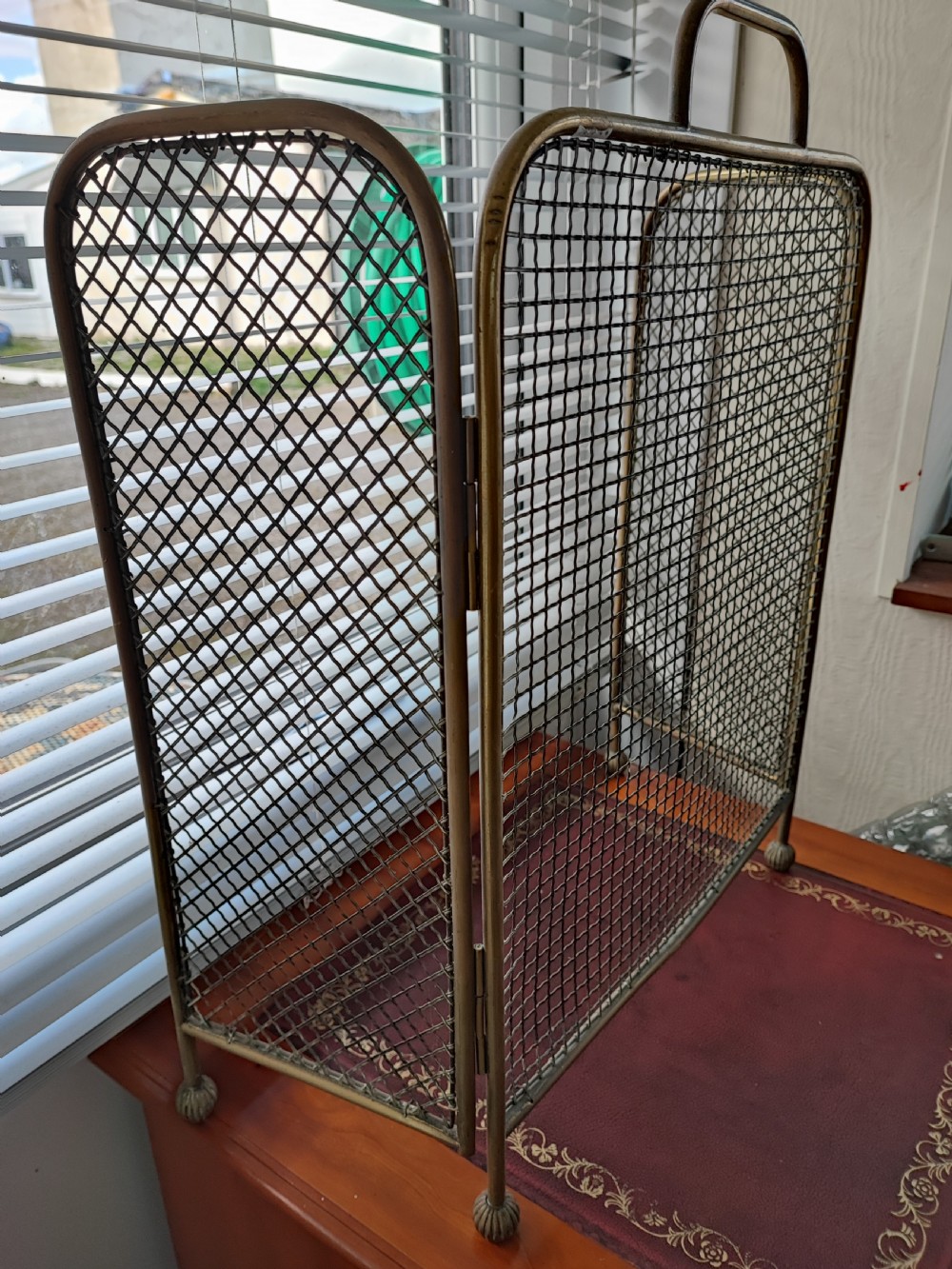 A Victorian brass spark guard featuring a central woven mesh panel with an arched handle, flanked by two hinged side wings on ball feet. View III