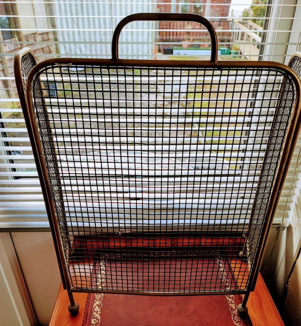 A Victorian brass spark guard featuring a central woven mesh panel with an arched handle, flanked by two hinged side wings on ball feet. View VII