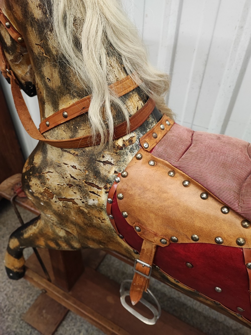 A large antique carved wooden rocking horse with a dappled painted finish, leather saddle, horsehair mane, and tail, mounted on a wooden safety stand. View II