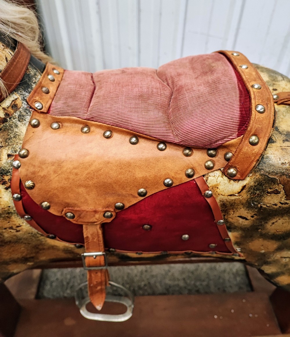 A large antique carved wooden rocking horse with a dappled painted finish, leather saddle, horsehair mane, and tail, mounted on a wooden safety stand. View V