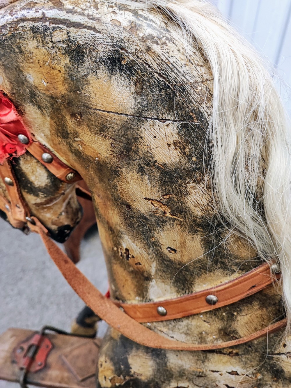 A large antique carved wooden rocking horse with a dappled painted finish, leather saddle, horsehair mane, and tail, mounted on a wooden safety stand. View VI