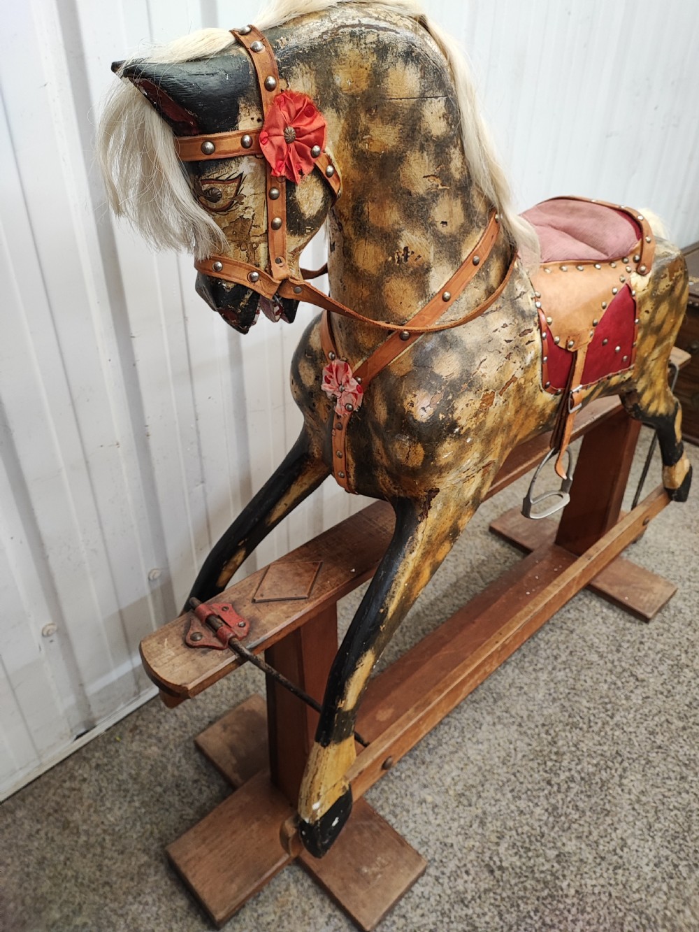 A large antique carved wooden rocking horse with a dappled painted finish, leather saddle, horsehair mane, and tail, mounted on a wooden safety stand. View XI