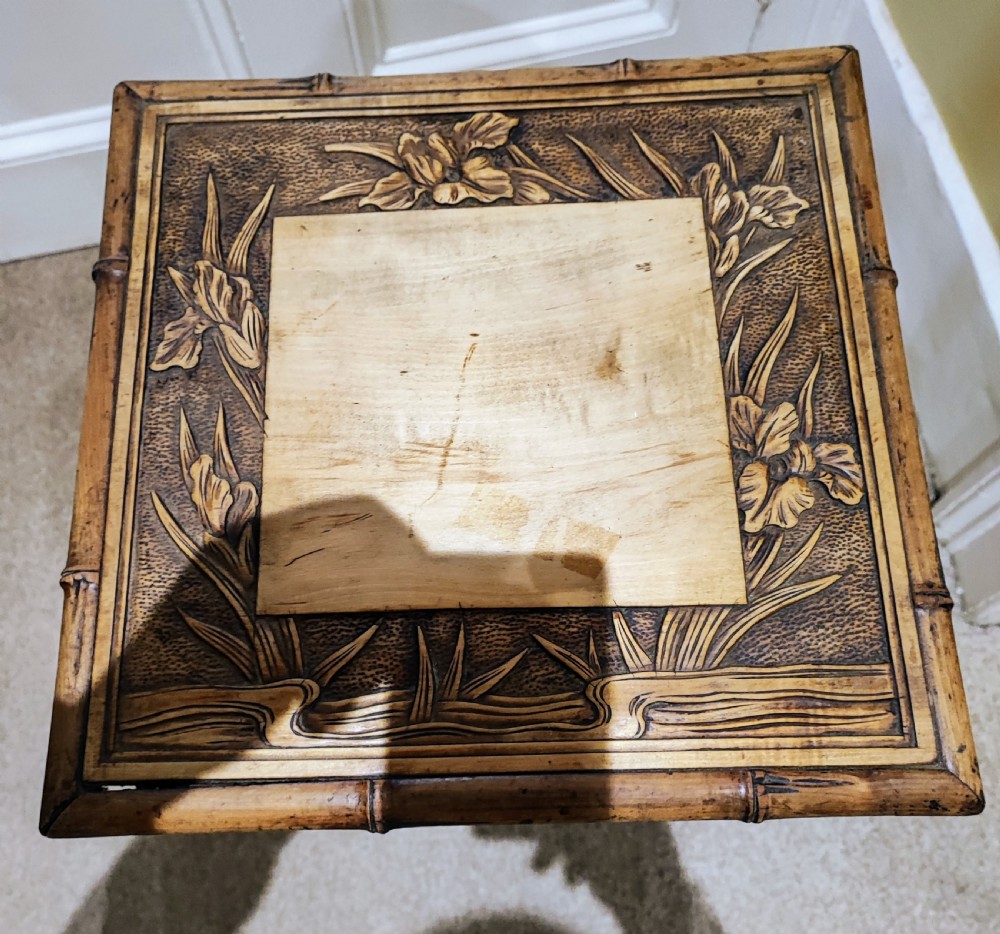 A square Arts and Crafts wooden side table featuring carved iris botanical motifs, bamboo-style edge moulding, shaped legs, and a carved lower shelf. View XI