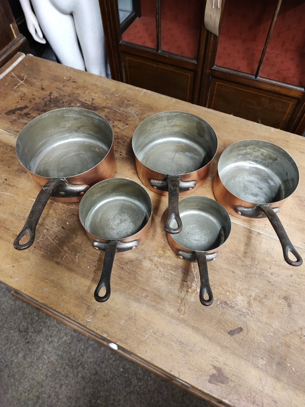 A set of five graduated antique copper saucepans with dark cast iron handles arranged upside down. View II