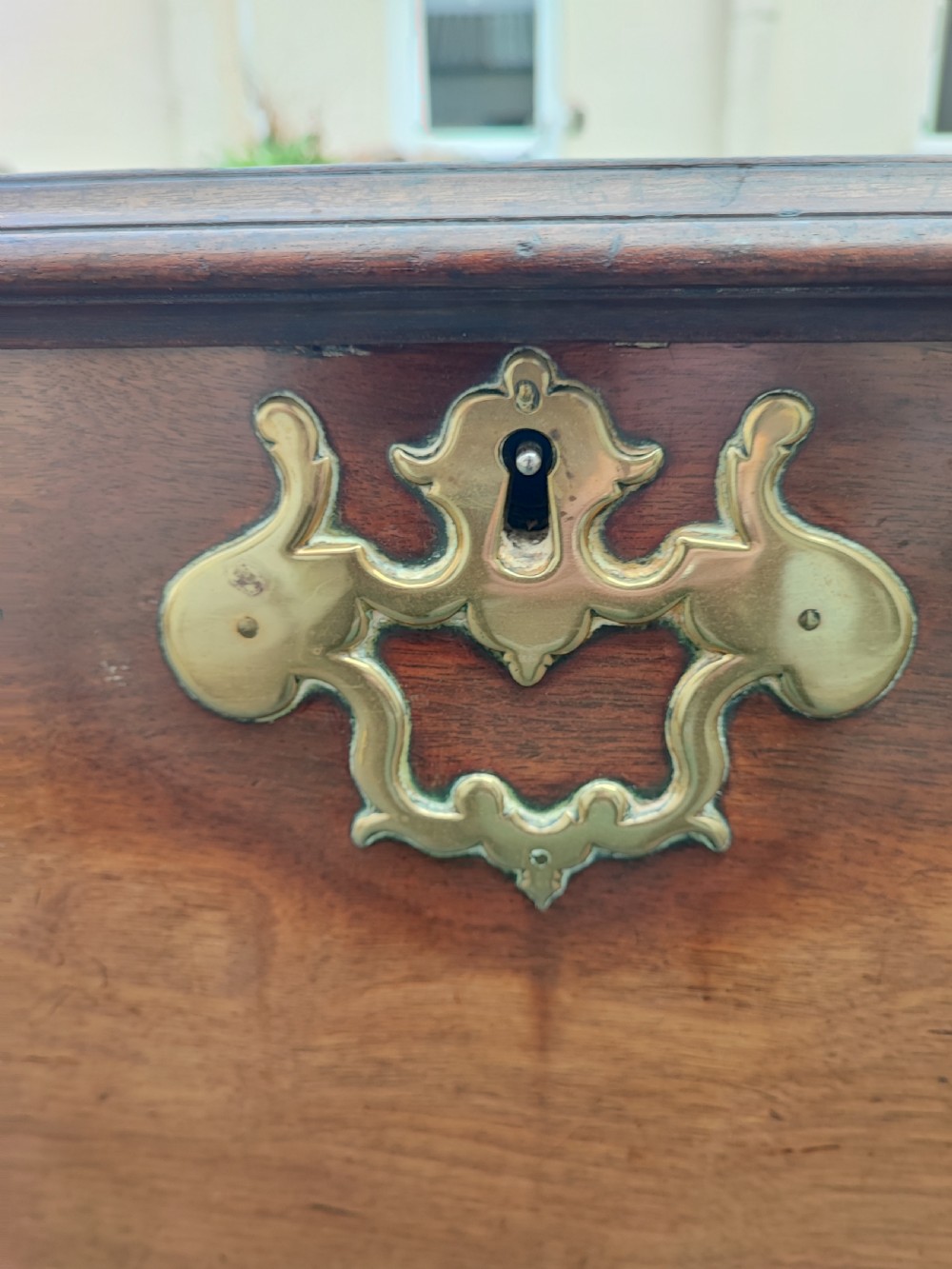 A George III mahogany storage trunk featuring a hinged top lid, two lower drawers, and brass batwing escutcheon handles. View X