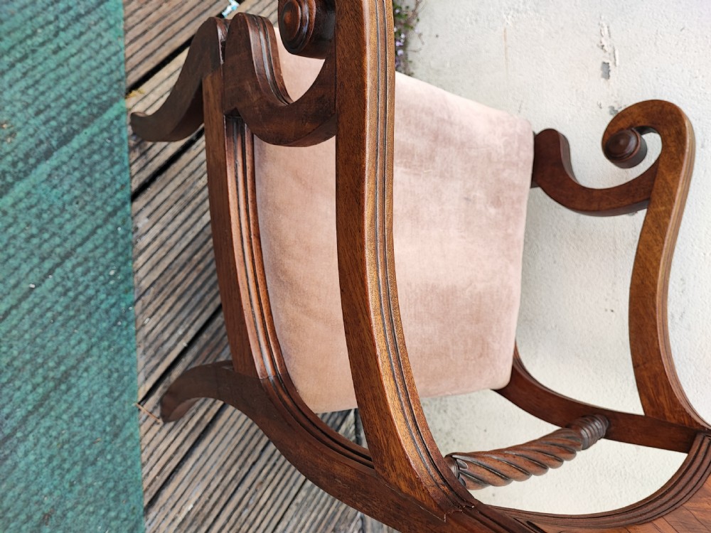 A side view of a Regency period mahogany armchair featuring carved scroll arms, sabre legs, and a padded seat. View V