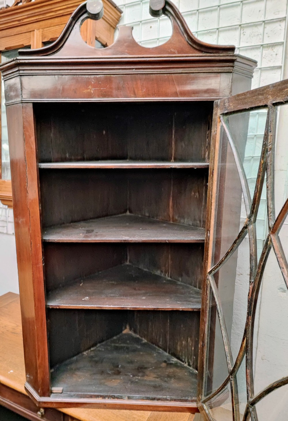 A Georgian mahogany hanging corner cabinet featuring a swan neck pediment, a single door with geometric astragal glazing, and internal wooden shelving. View III