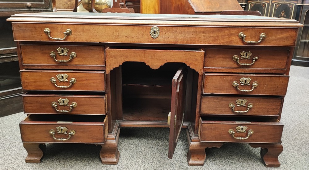 An eighteenth-century Georgian mahogany kneehole desk featuring a leather writing surface, multiple drawers with brass handles, a central recessed cupboard, and bracket feet.