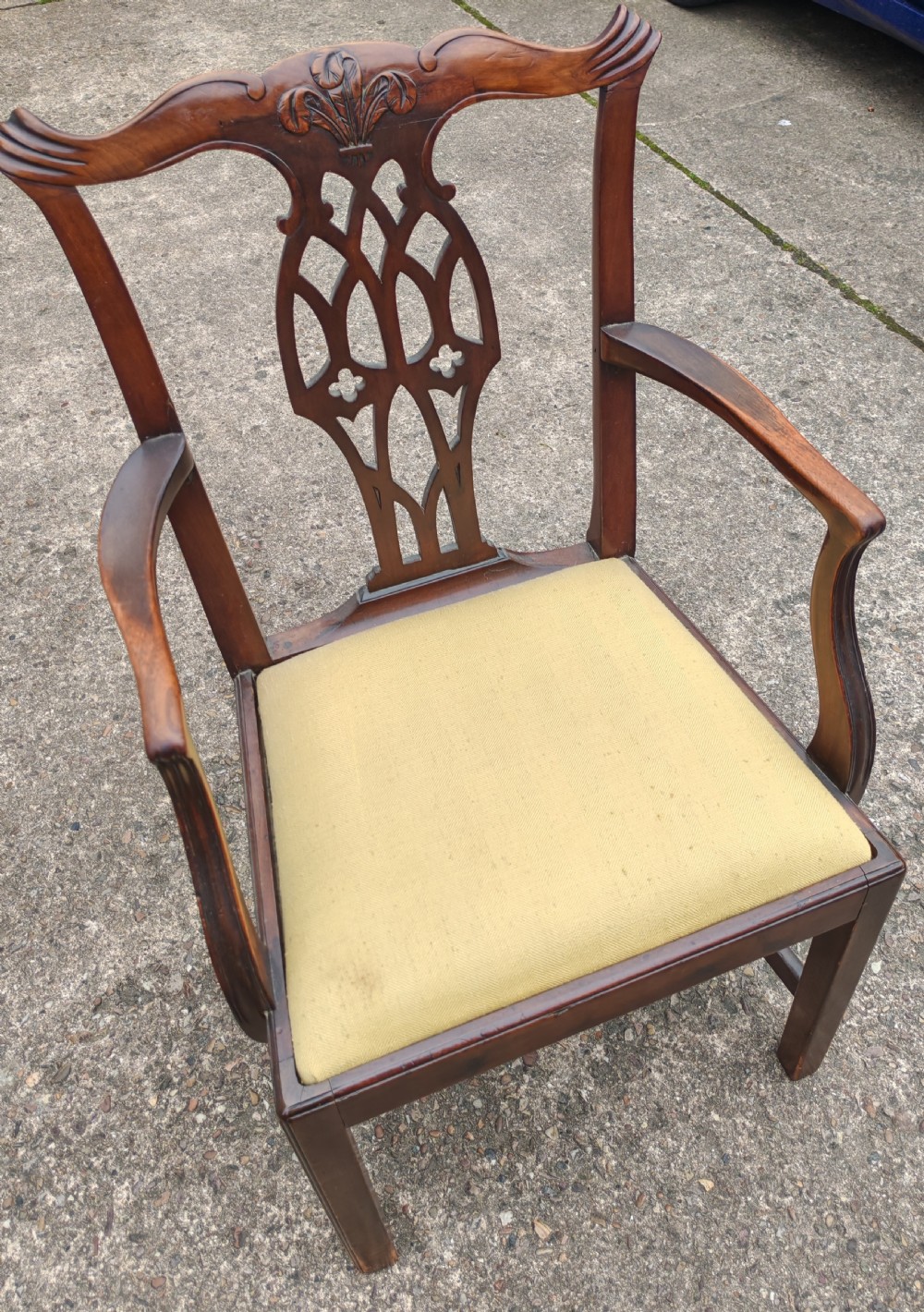A Georgian mahogany carver armchair featuring a carved pierced back splat, swept arms, and a light yellow drop-in seat cushion.