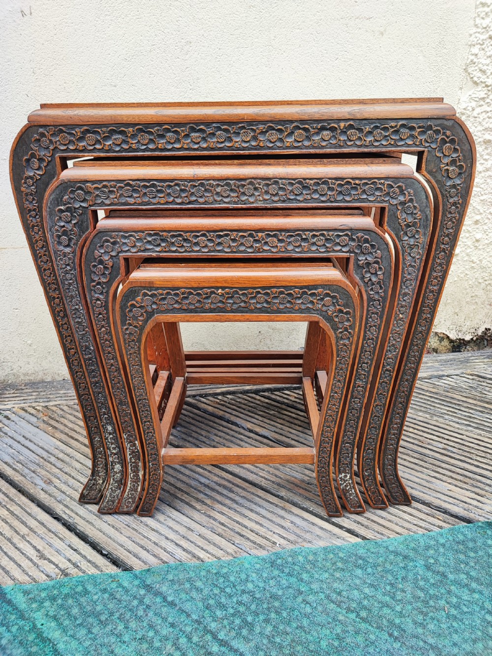 A set of four graduated dark hardwood nesting tables featuring hand-carved floral borders along the aprons and curved legs.