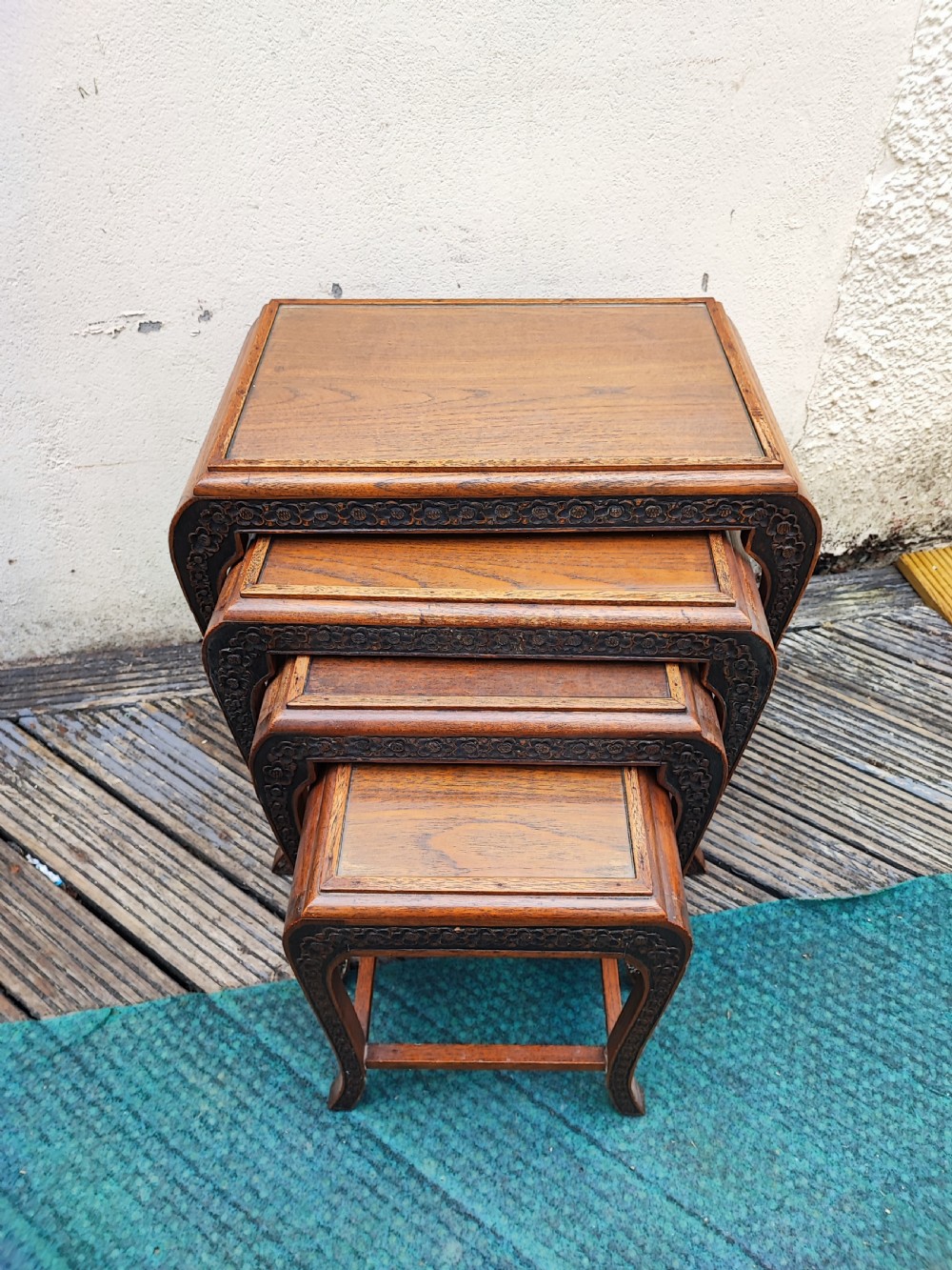 A set of four graduated dark hardwood nesting tables featuring hand-carved floral borders along the aprons and curved legs. View III