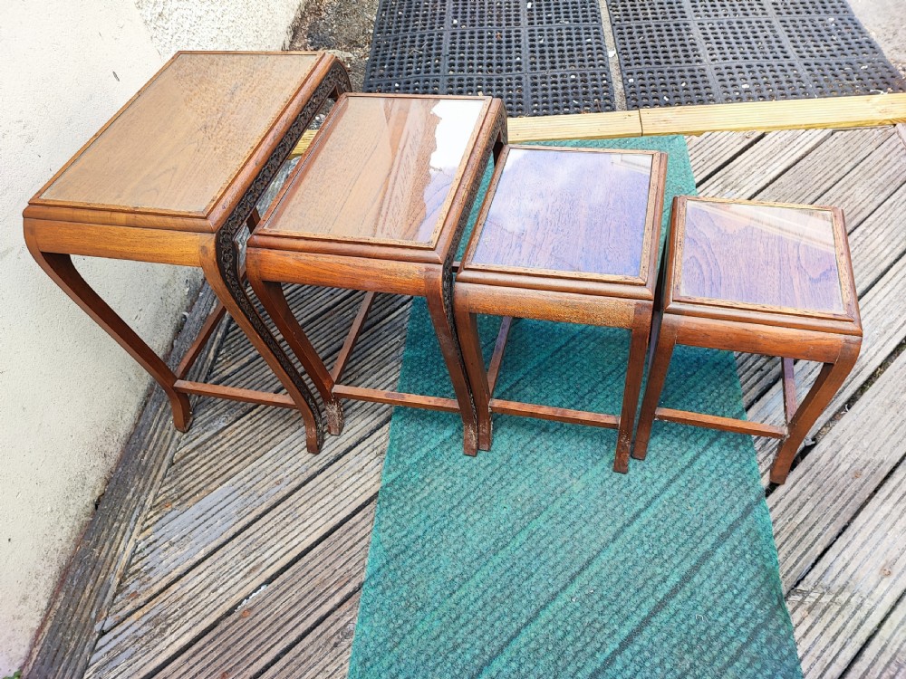 A set of four graduated dark hardwood nesting tables featuring hand-carved floral borders along the aprons and curved legs. View V