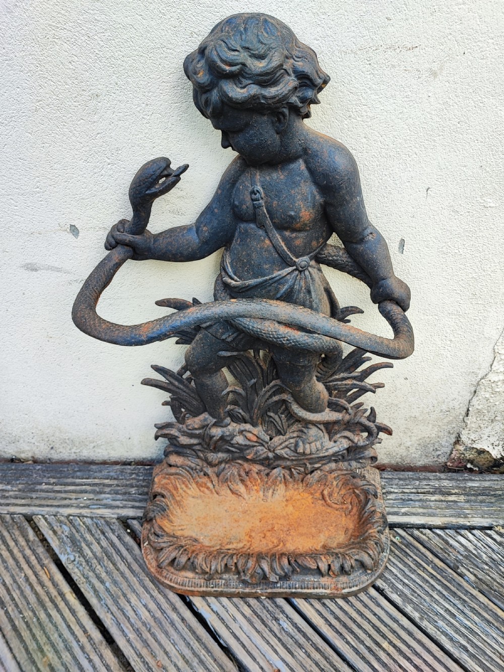 A Victorian cast iron stick stand featuring a figure of a young boy holding a serpent on a leafy base with an integrated drip tray.