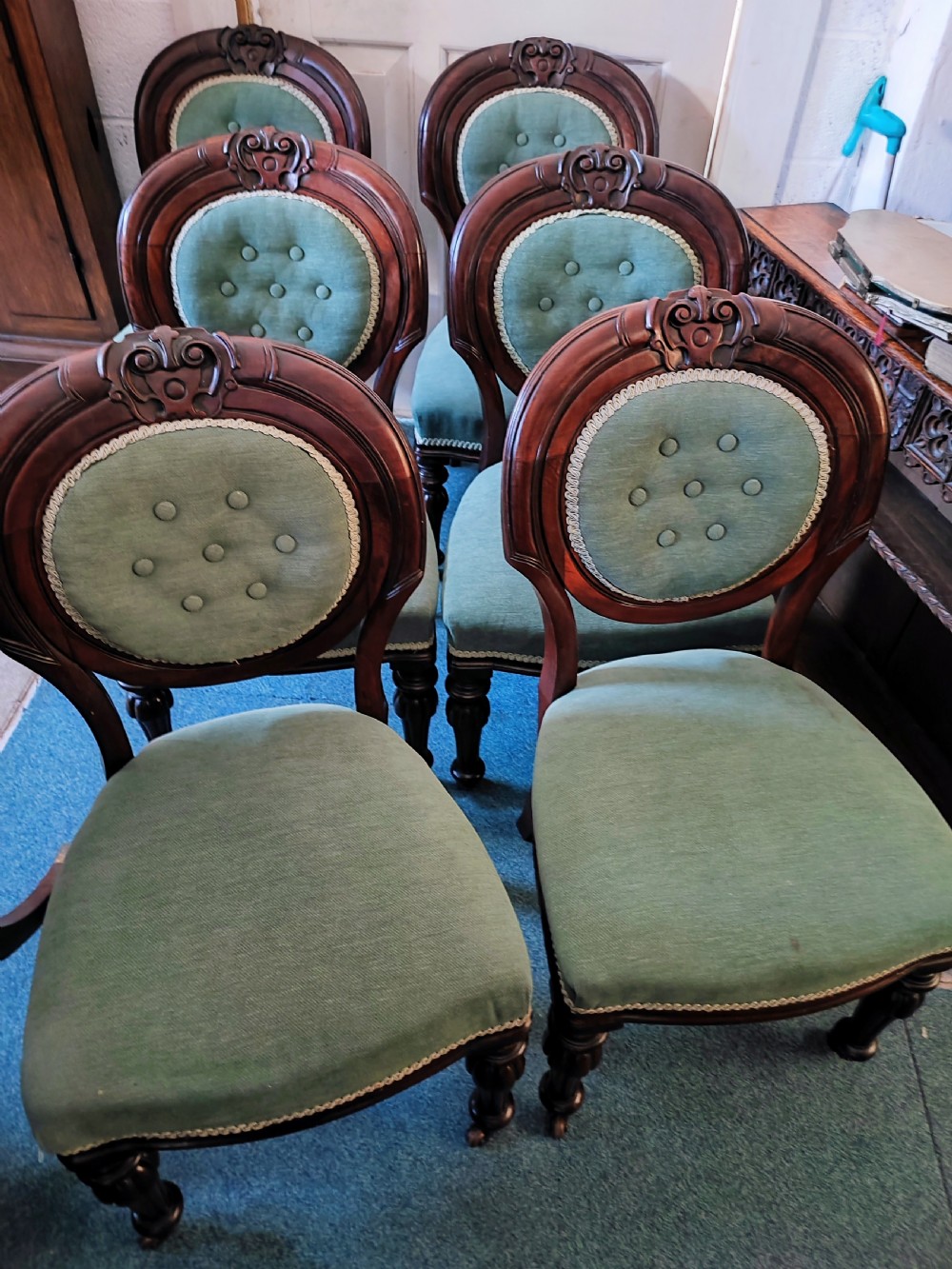 A set of six Victorian mahogany dining chairs featuring carved balloon backs, green buttoned upholstery, and turned front legs.