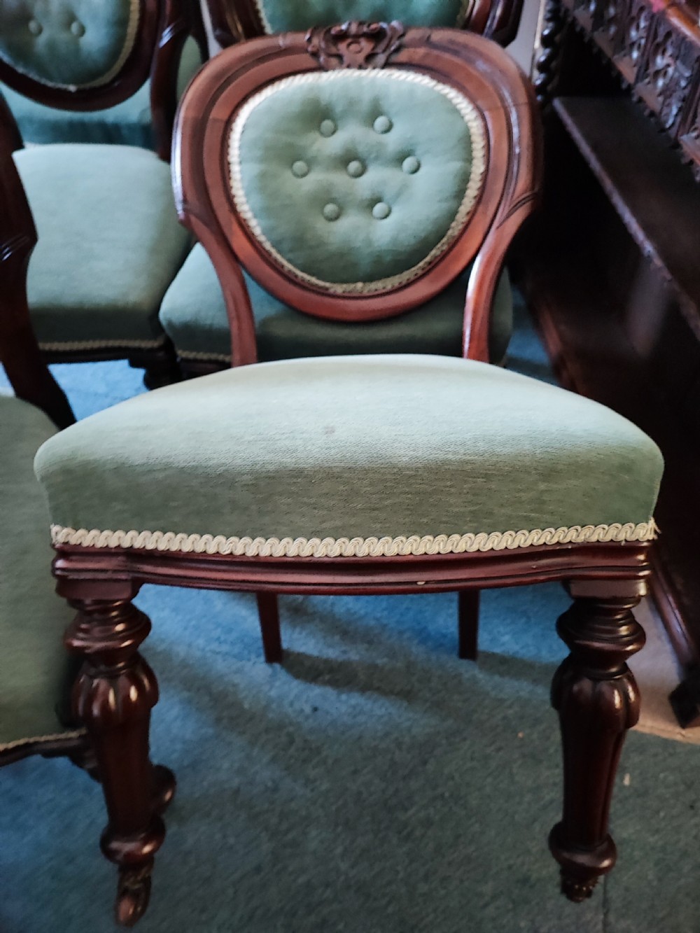 A set of six Victorian mahogany dining chairs featuring carved balloon backs, green buttoned upholstery, and turned front legs. View X