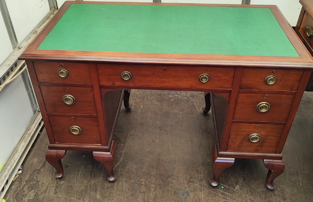 An Edwardian mahogany kneehole writing desk featuring a green leather inset top, brass ring handles, and cabriole legs.