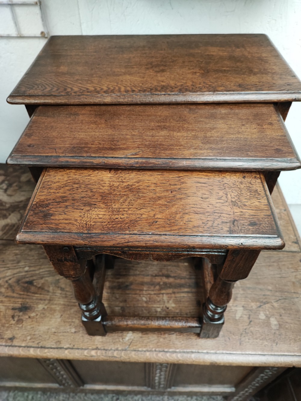 A set of three graduated dark oak nesting tables featuring turned legs and moulded top edges stacked together.