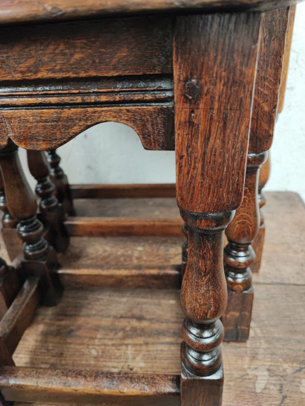A set of three graduated dark oak nesting tables featuring turned legs and moulded top edges stacked together. View II