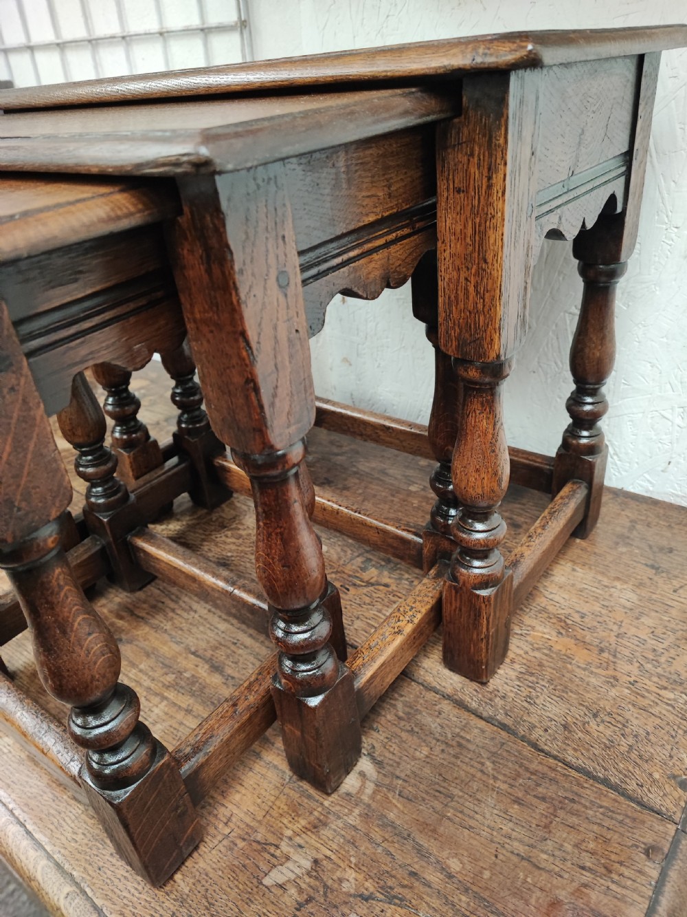 A set of three graduated dark oak nesting tables featuring turned legs and moulded top edges stacked together. View V