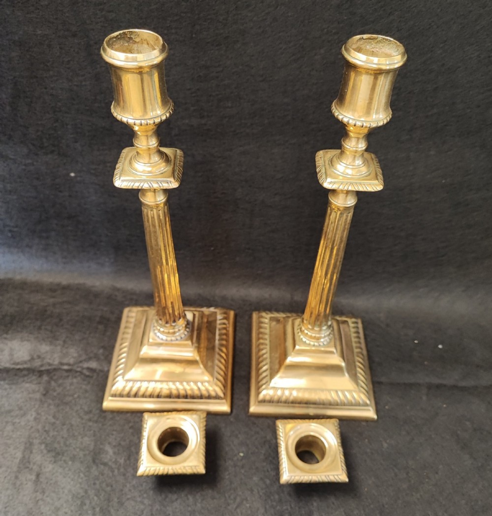 A pair of Georgian brass candlesticks featuring fluted columns, square stepped bases with gadrooned trim, and removable square nozzles.