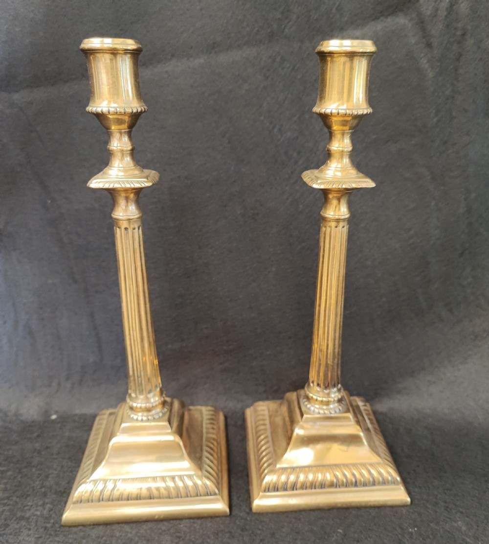 A pair of Georgian brass candlesticks featuring fluted columns, square stepped bases with gadrooned trim, and removable square nozzles. View III