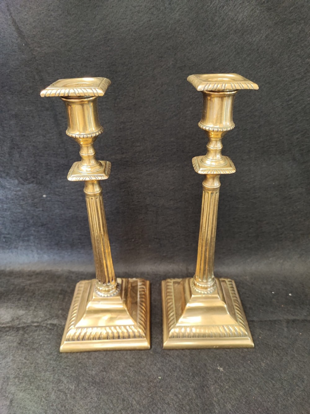 A pair of Georgian brass candlesticks featuring fluted columns, square stepped bases with gadrooned trim, and removable square nozzles. View V
