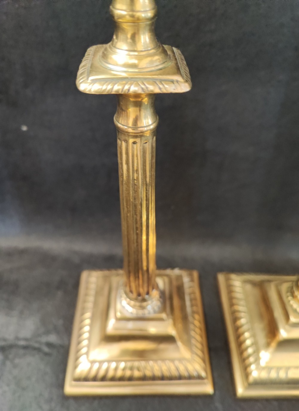 A pair of Georgian brass candlesticks featuring fluted columns, square stepped bases with gadrooned trim, and removable square nozzles. View VI