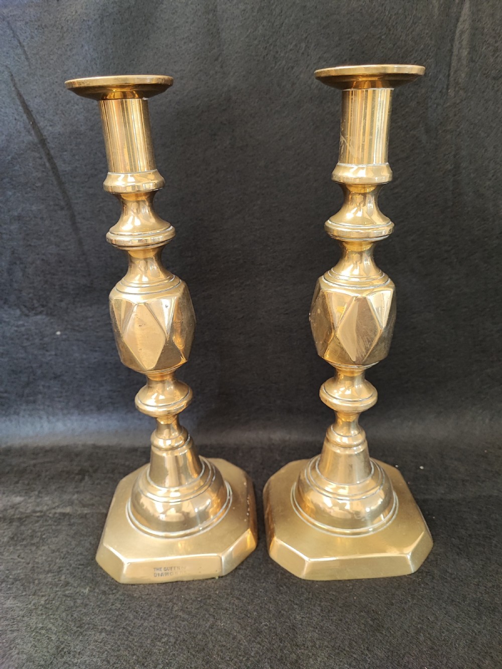 A pair of polished Victorian brass candlesticks featuring diamond-faceted central knops and octagonal stepped bases stamped with maker details.