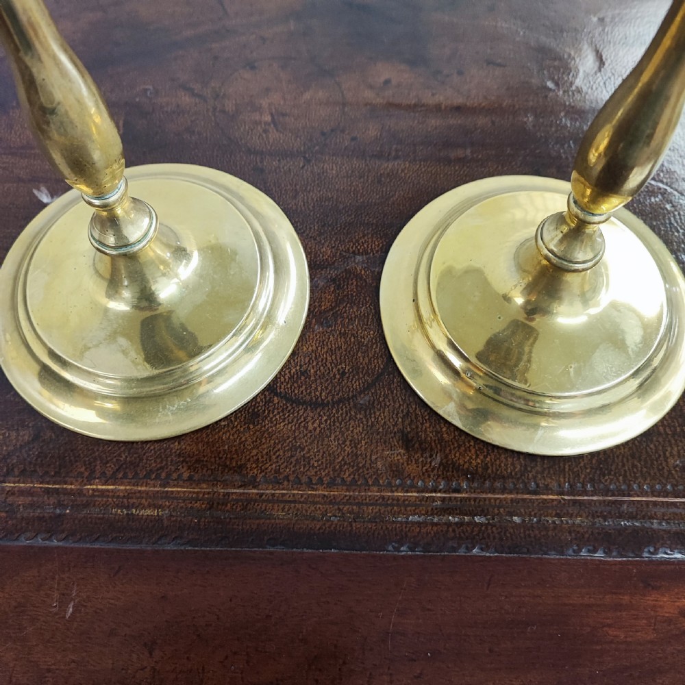A matching pair of 19th-century cast brass candlesticks featuring turned baluster stems, circular drip pans, and stepped round bases. View V