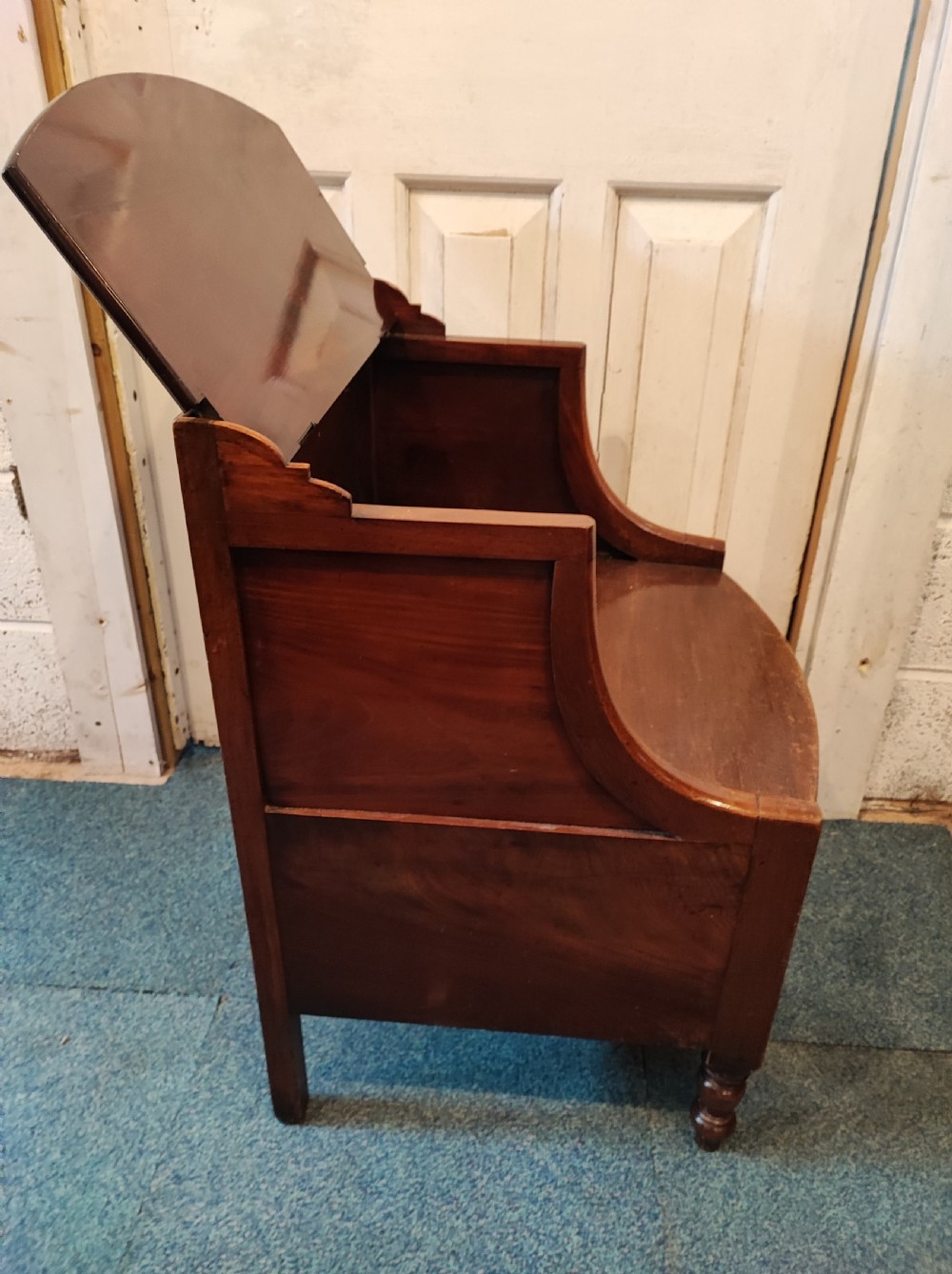 An antique Regency flame mahogany bedside commode with a top shelf tier, a stepped middle surface, and a curved front raised on turned feet. View V