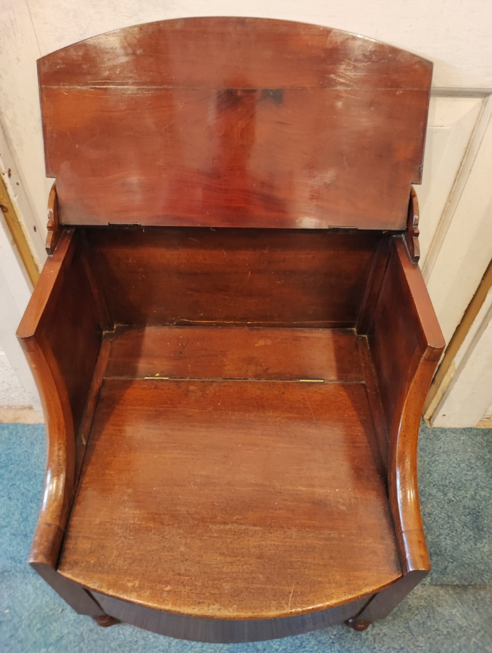 An antique Regency flame mahogany bedside commode with a top shelf tier, a stepped middle surface, and a curved front raised on turned feet. View VI
