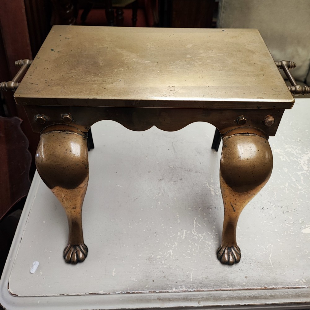 A Georgian brass hearth footman featuring a smooth rectangular top, side drop handles, a scalloped apron, and front cabriole legs with paw feet.